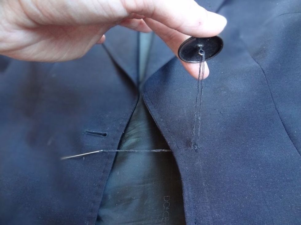 Loop your thread through the round hook of the button and then back into the fabric of the top side of the coat. Try to stay as close to the prior button holes as possible.