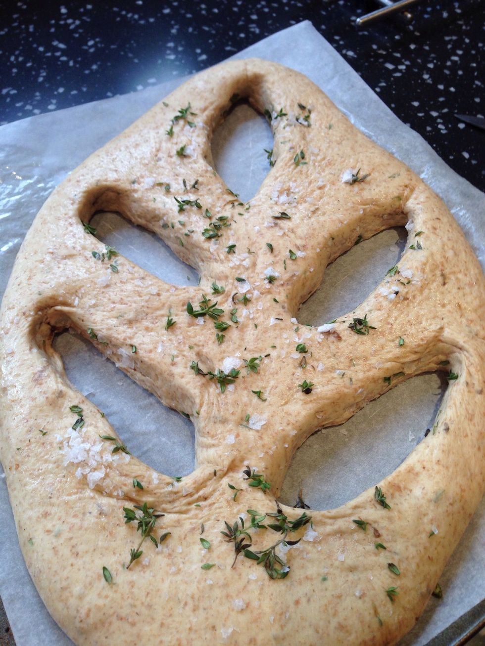 Make 5 slits in the dough in a leaf shape. Use your fingers to widen them slightly. Carefully slide the paper with the dough on it onto the heated baking stone or upturned baking tray.