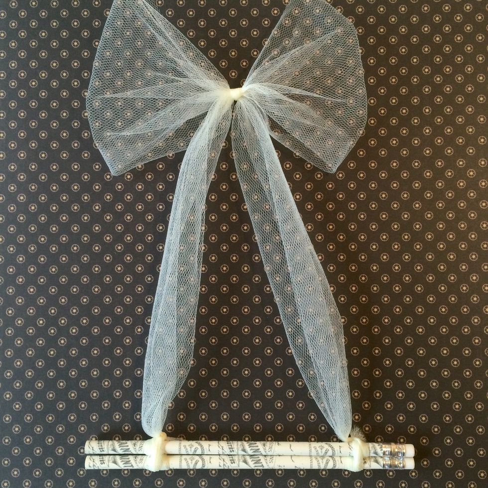 Make a bow in the center of the 4 ft length of tulle. Take one end of the tulle and wrap it around the ends of two decorative pencils, and then do the same on the other end.