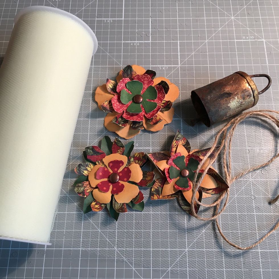 Make a bow using tulle. Make or use pre made paper flowers. Choose one or two decorative bells. Arrange and attach to board.