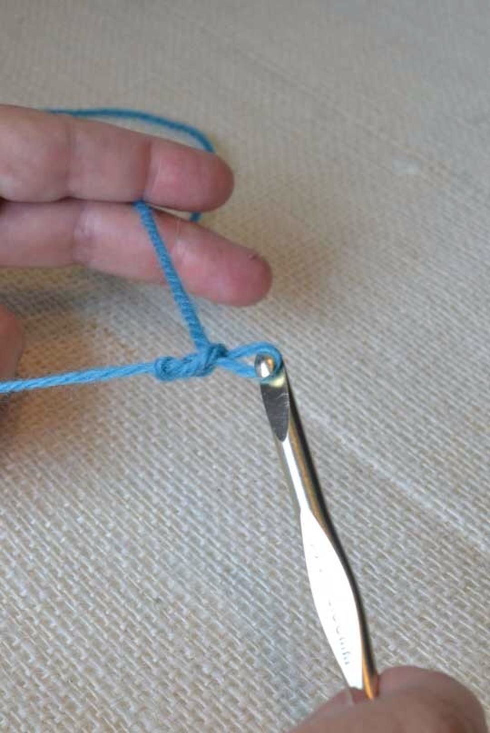 Make a Foundation Chain. Holding the slipknot in place with your right pointer finger, use your left hand to wrap the ball end of the yarn behind the hook, clockwise, & over the throat of your hook.