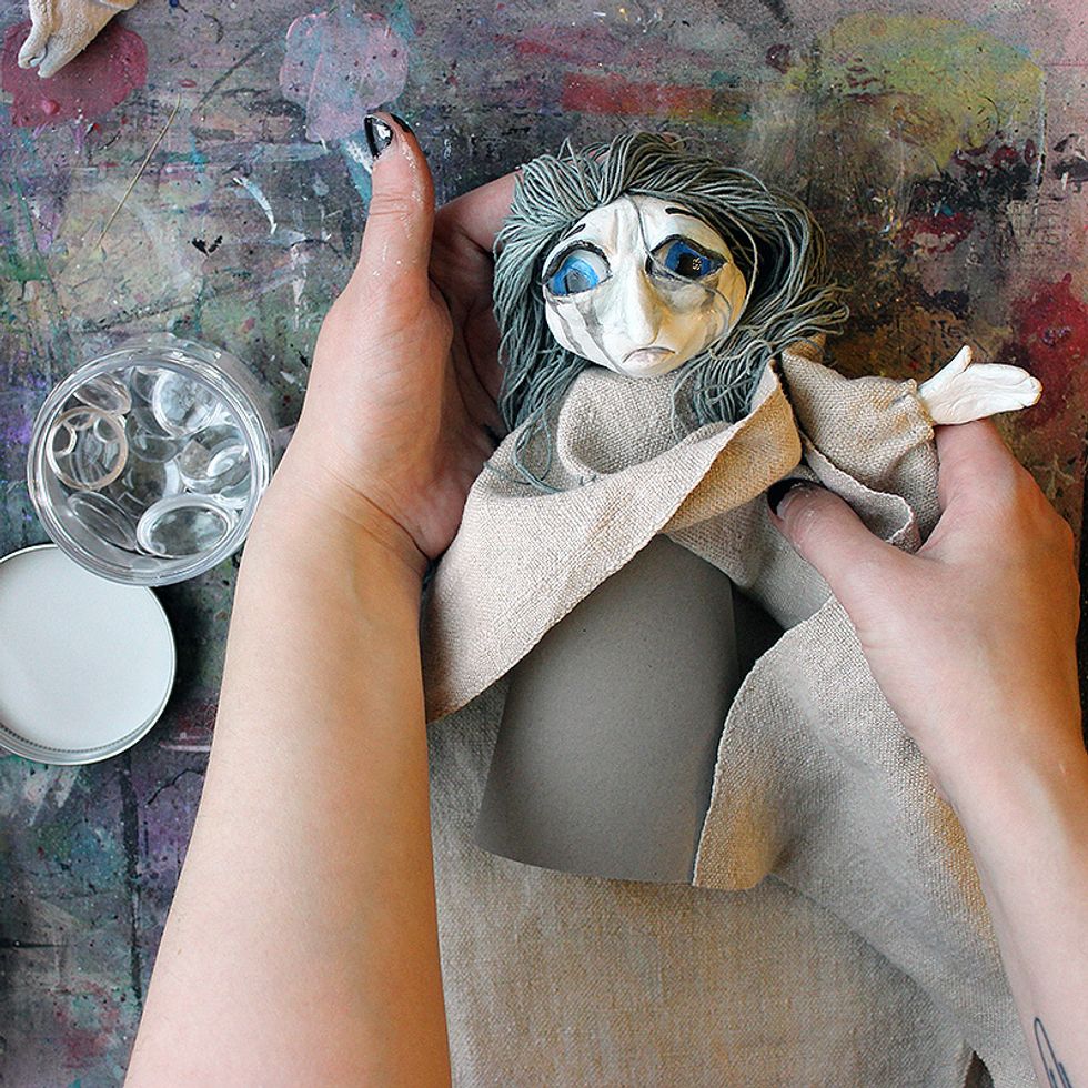 Make your art doll. Use clay, cloth, cardboard and twine or any other material you wish. I made my doll's eyes using Prima Pebbles.