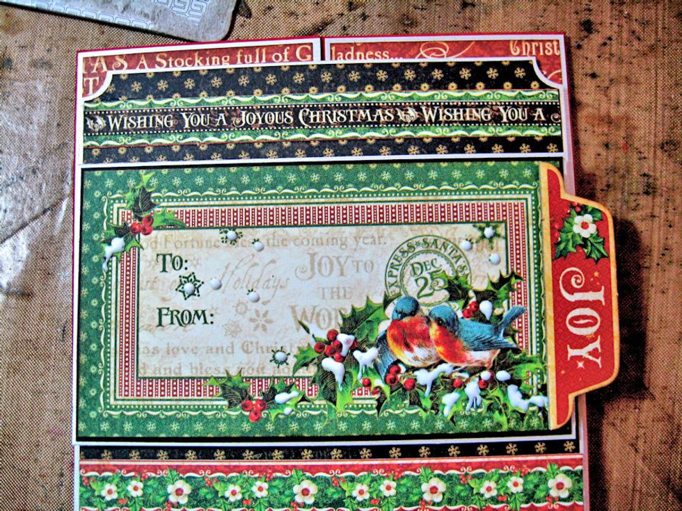 Mat focal image on black and silver cardstock. Glue JOY chip on the right. Glue waste chipboard or foam tabs on back and attach to center of medallion as seen here. Add glue to snowy parts of image