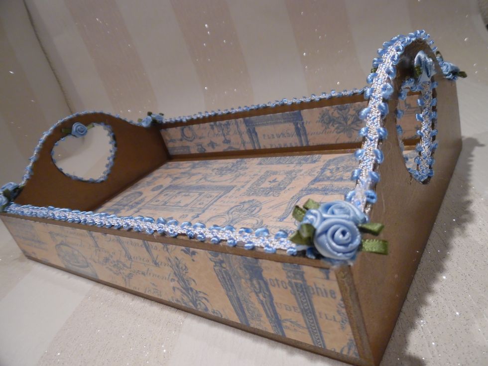 MDF tray was painted gold. Covered in blue themed Gilded Lily paper. Tray was then sealed using decoupage varnish. Trimmed in blue & white braid and satin roses. Finished with a sprinkle of glitter.