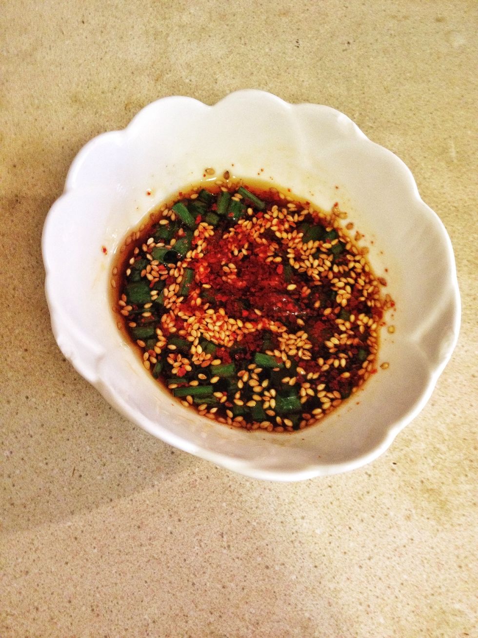 Meanwhile you're gonna prepare the dipping sauce. Add 1 tbsp soy sauce with drizzle of sesame oil and 1/2 tbsp vinegar. Put in chopped green scallions, roasted sesame seed, red pepper powder and mix.