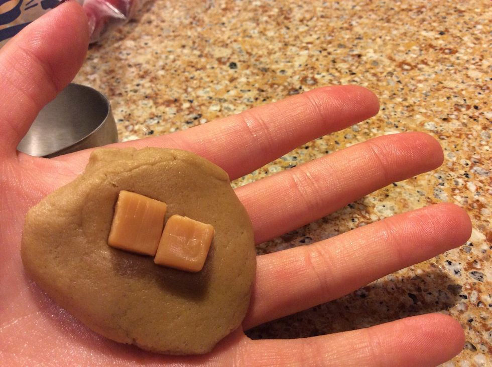 Measure about 1 1/2 tablespoons of the dough into a ball. Flatten the ball with the palm of your hand, then place one of the caramel pieces in the center. Wrap the dough completely around the square.