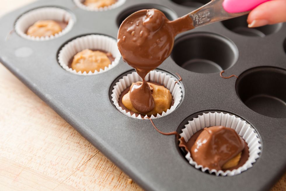 Melt the remaining chocolate in the microwave. Pour about 1\u00bd tsp of melted chocolate into each cup, covering the peanut butter filling. Then, gently bang the tin on your counter to even out the tops.