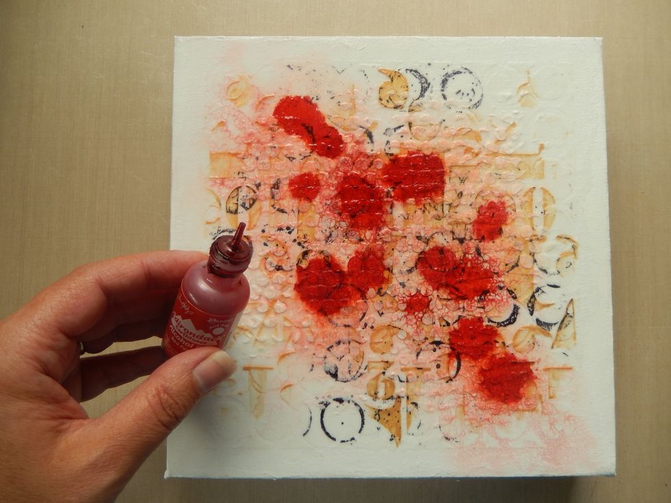 Mist the whole canvas with water before dripping drops of Red Pepper Alcohol Ink diagonally across the stencilled area of the canvas. Mist with more water to allow the ink to seep into the cracks.