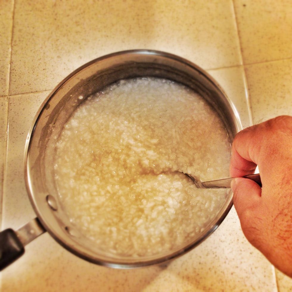Mix the cooked rice and chicken stock together. Cook over a small fire stirring consistently till a porridge forms. Add water if necessary. It should resemble Grits.