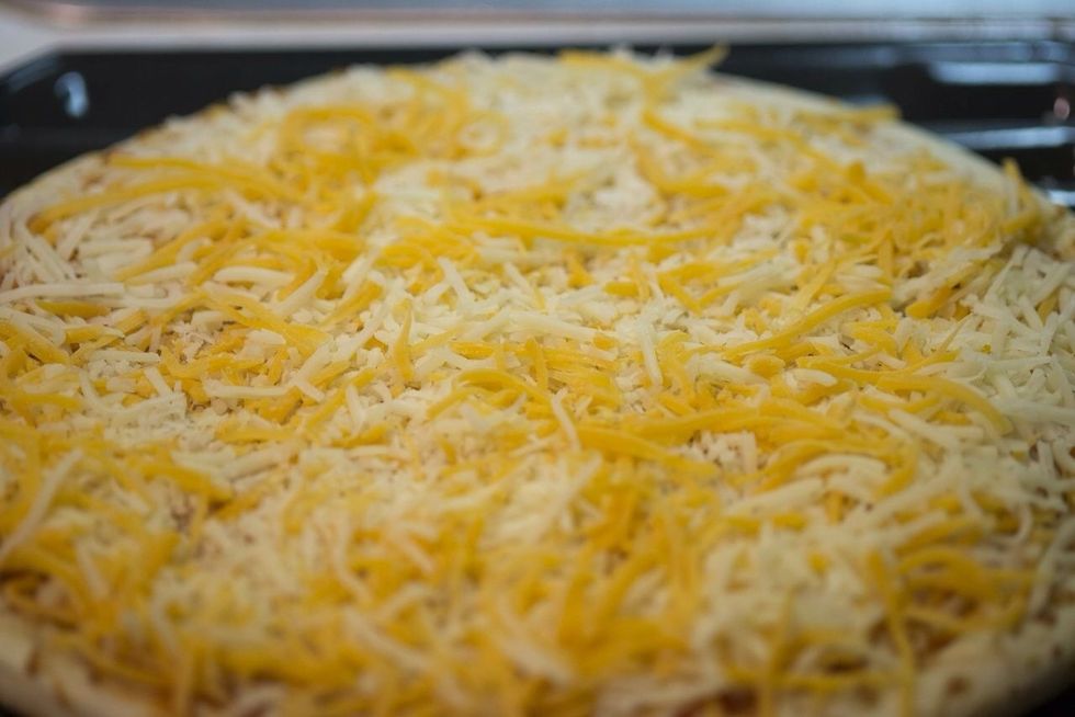 Mix the mozzarella cheese and the cheddar cheese together and spread evenly over the sauce. Remember to keep the lip of the dough clear.