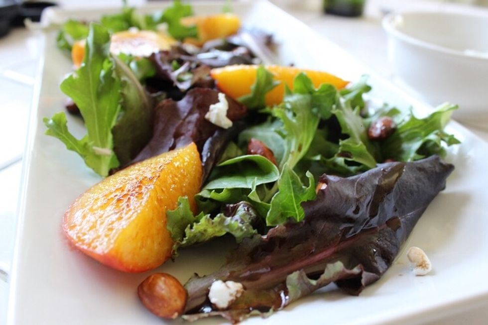 Mix the toasted almonds into the salad, finish with four peach slices & drizzled balsamic vinegar.