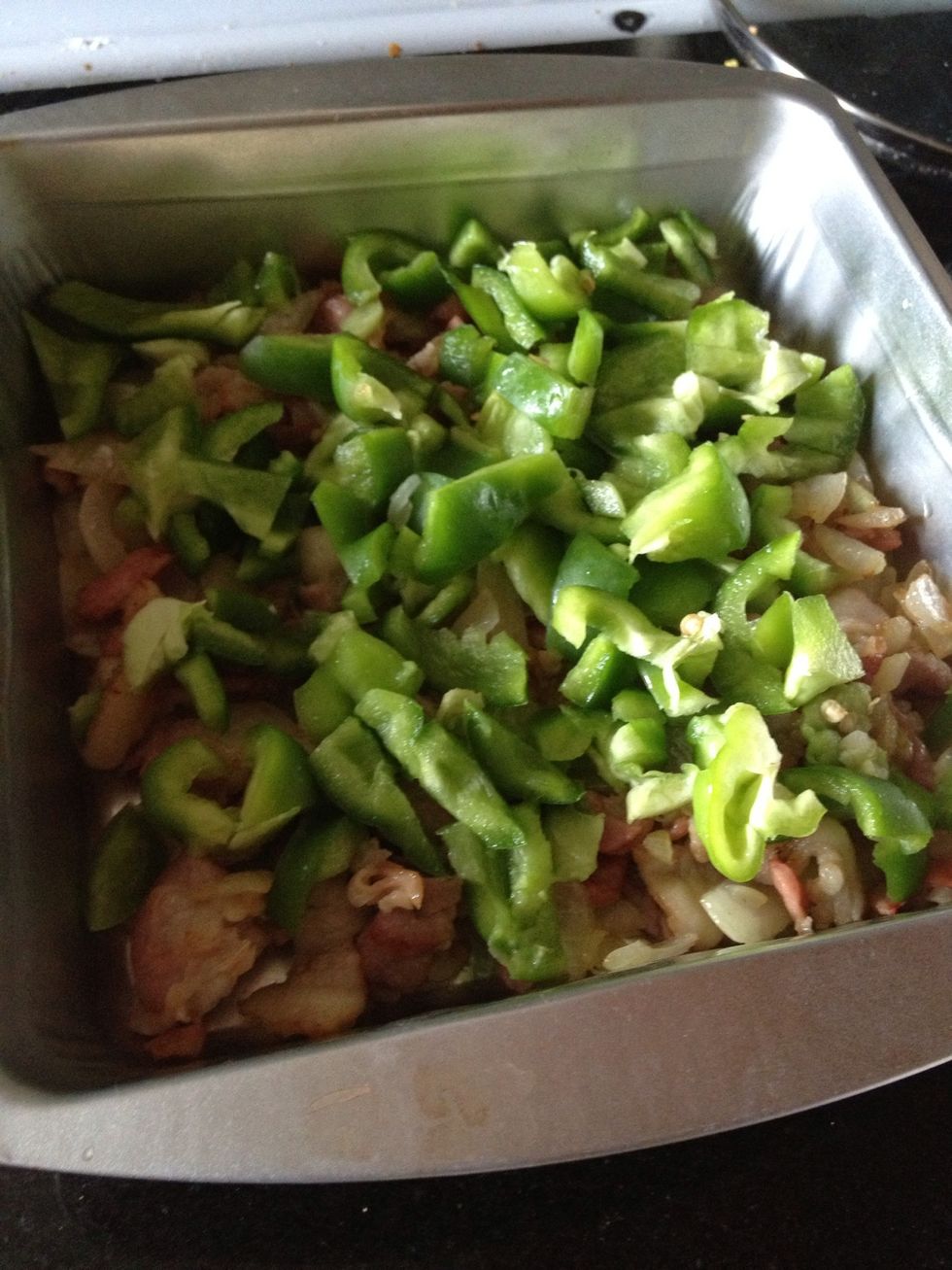 Move fried onions and meat to the baking pan and set aside. Remove seeds and stem from the green pepper and dice it; cover meat and onions with layer of diced green pepper.