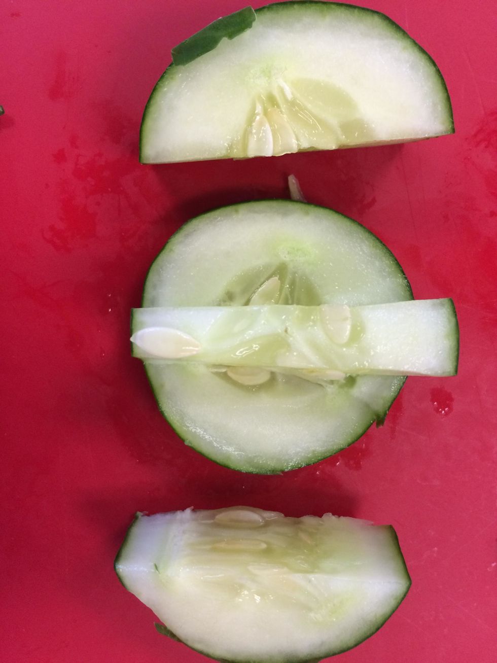 move onto the other piece you cut off from the cucumber and leave about a half inch in the center and on both side cut down into it but not all the way and then finish cutting it off from the sides