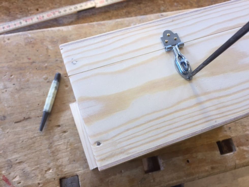 N\u00e4r \u00f6verdelen \u00e4r klar s\u00e5 placera "\u00f6glan" enligt bild och g\u00f6r ett h\u00e5l med syl i nedersta h\u00e5let enligt bild. F\u00e4ll upp haspen och spika fast och g\u00f6r sen n\u00e4sta h\u00e5l och spika.