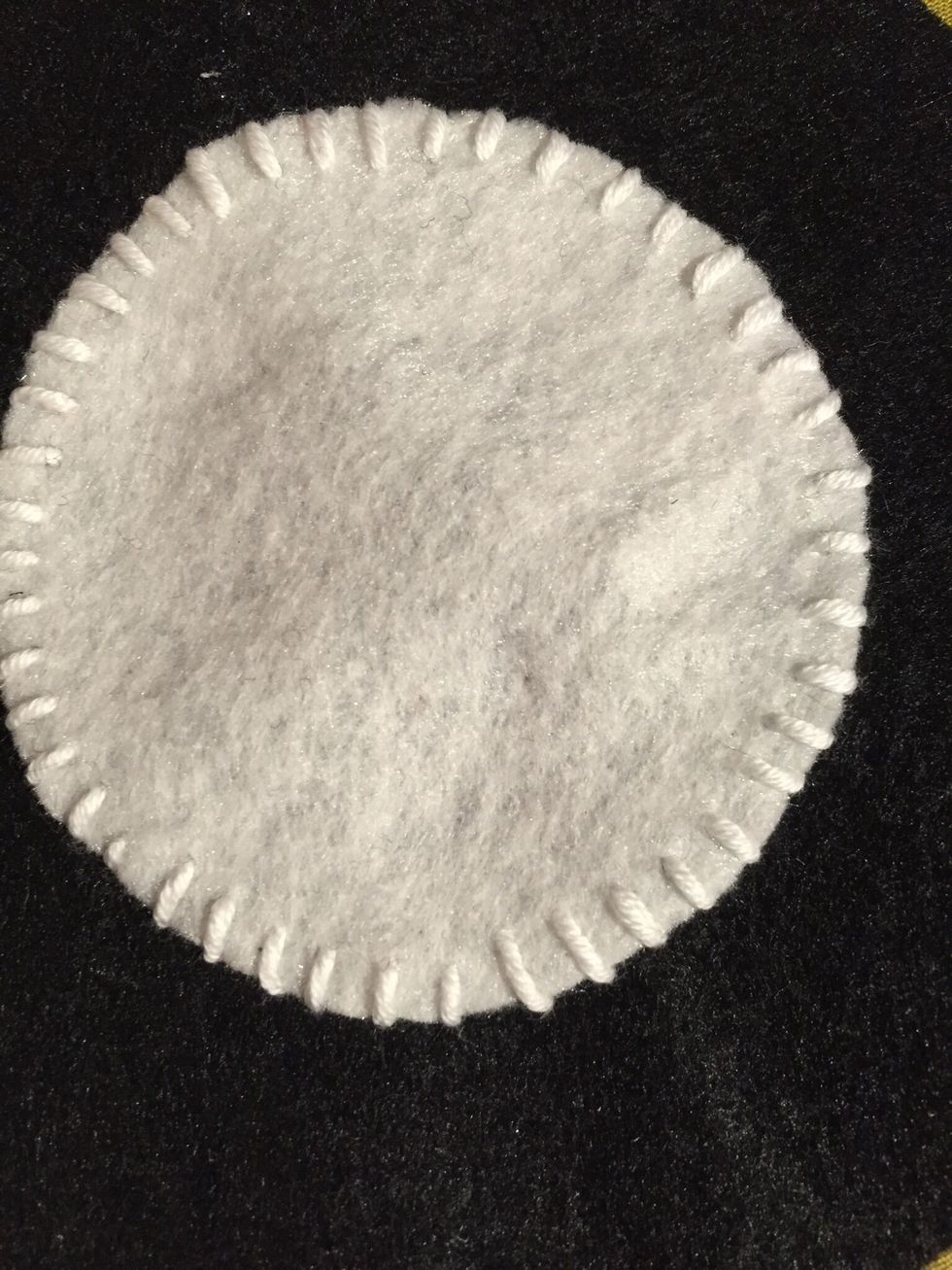 N\u00e5la fast den lilla vita cirkeln mitt i den svarta. Sy fast den med KASTSTYGN. Se till att knuten hamnar p\u00e5 baksidan n\u00e4r du b\u00f6rjar sy. Gl\u00f6m inte att f\u00e4sta tr\u00e5den n\u00e4r du sytt runt. F\u00e4st p\u00e5 baksidan.