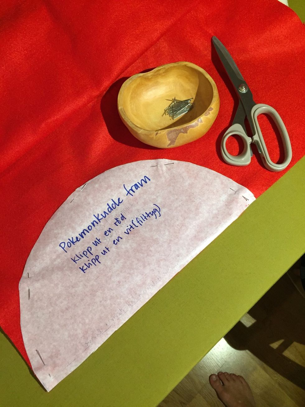 N\u00e5la fast halvcirkeln p\u00e5 r\u00f6tt tyg. Klipp ut.