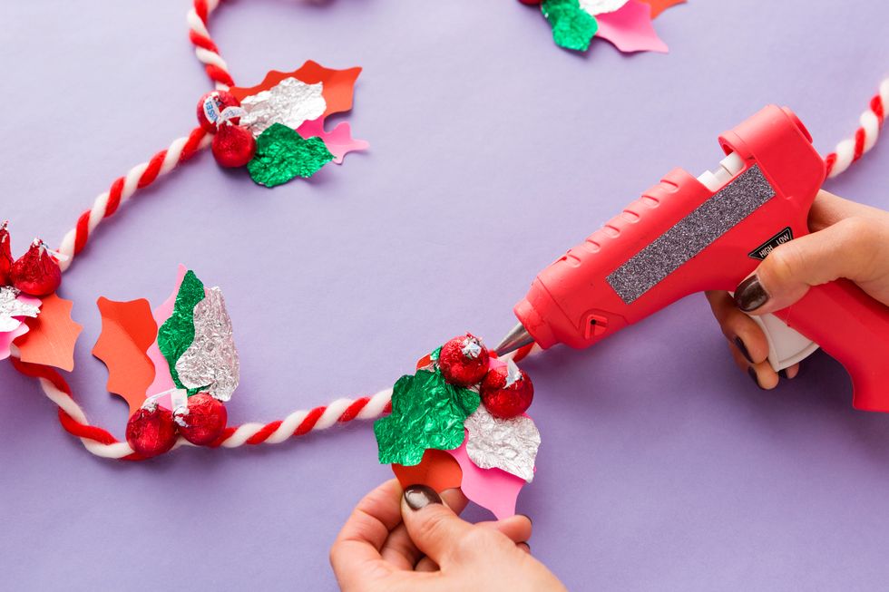 Next, attach your holly bunches to a colorful string. If you\u2019re doing this project with kids, you\u2019ll want an adult to use the hot glue gun for ultimate safety.