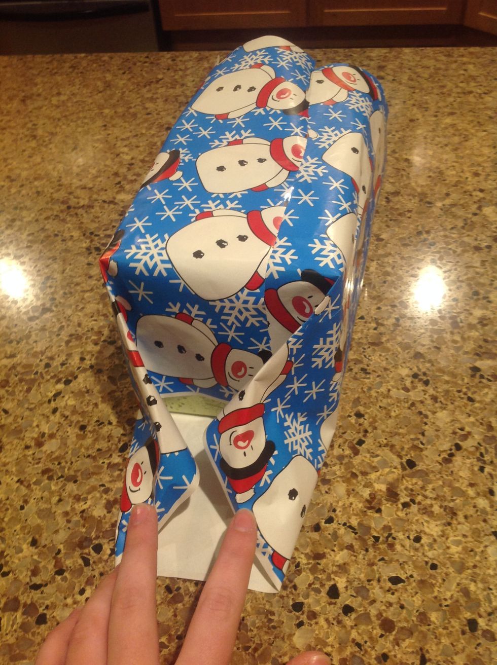 Next, begin to fold in the extra paper at the ends of the box like so. Bring the sides to the bottom of the gift.