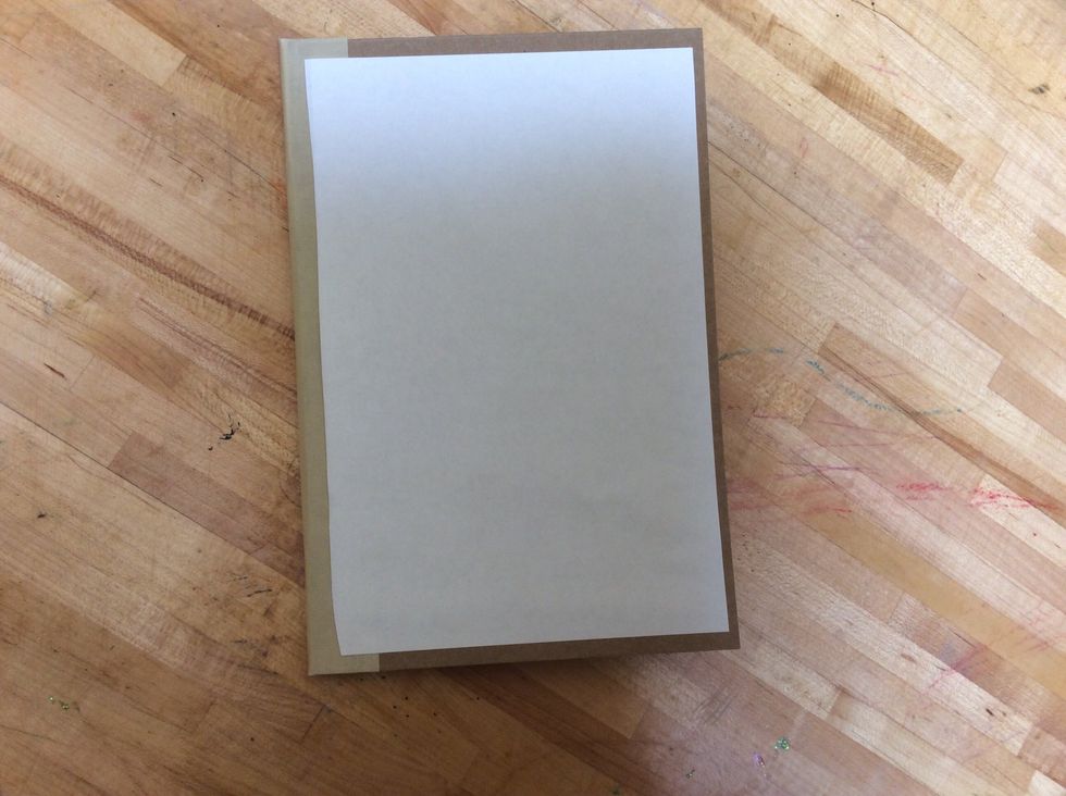 Next, center the piece of paper (glue side down) in the middle of the front of your book cover.  When you put it down rub and smooth the paper hard enough so that it sticks to the cardboard.
