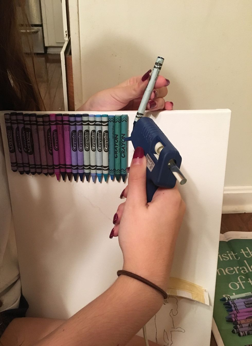 Next, choose the order and color for your crayons. Green, blue, and purple work best for the rain effect. You're going to glue them across the top of the canvas with the glue gun.