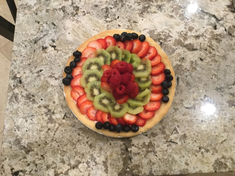 Next, cut the kiwis in thin slices and place them in a circle, place another circle of strawberries, then take the blueberries to fill any space you see, then cluster the raspberries in the middle.