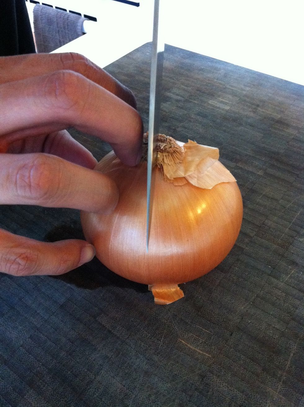 Next flip the onion onto the top side you just cut off and cut the onion in half right down the middle of the root. The root will keep both halves intact