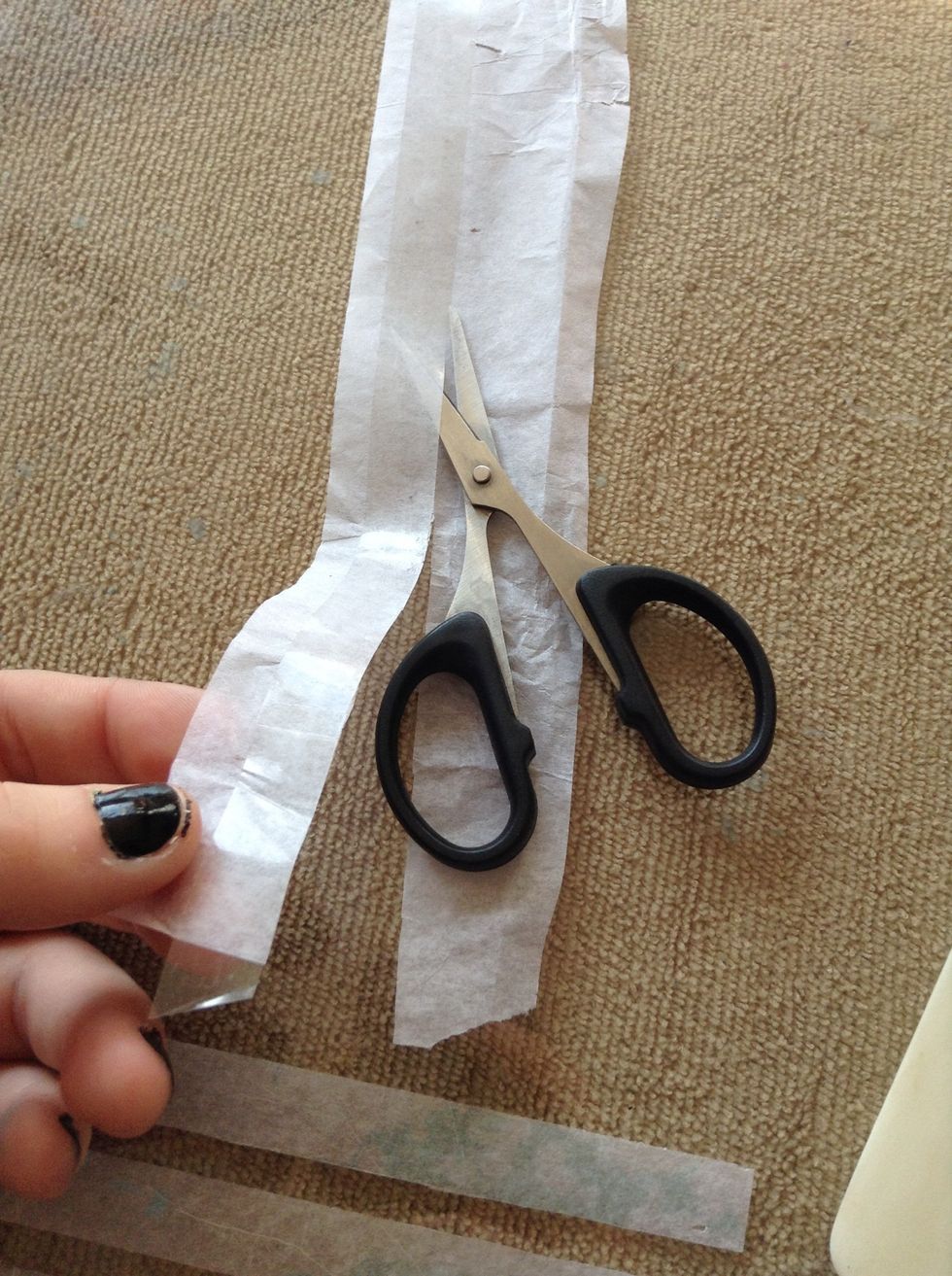 Next, flip the tissue paper over so the tape is facing up. Take your scissors and cut along the line of the tape, trimming the extra tissue paper off.