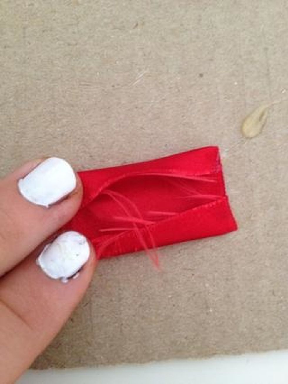 Next, lay the piece of ribbon as shown and place hot glue on the top and bottom of the ribbon. Then, fold the top and the bottom of the ribbon and place it on the hot glue as shown in the picture.