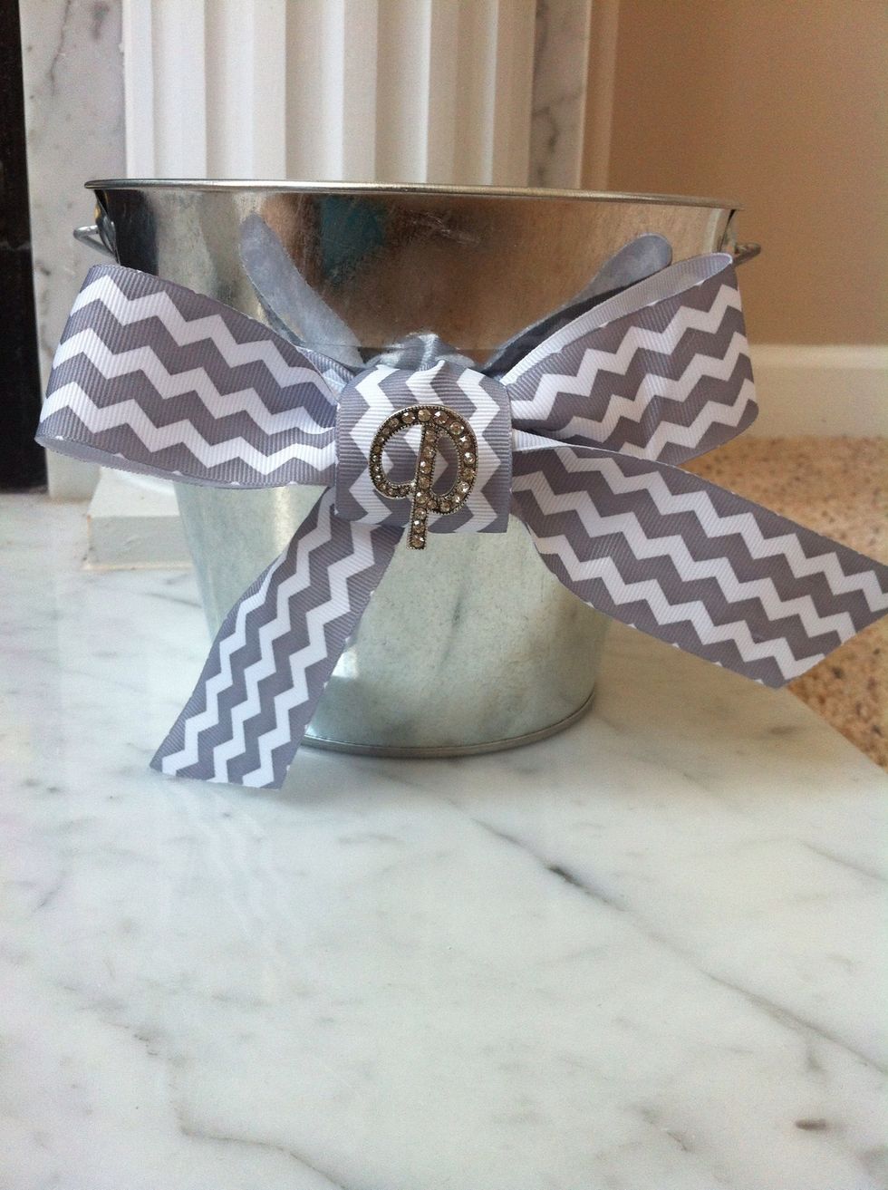 Next, line the ribbon carefully with hot glue. Once you have done that, place the ribbon onto the silver bucket and tie it into a bow. ( I added a cute little initial broach from Hobby Lobby)