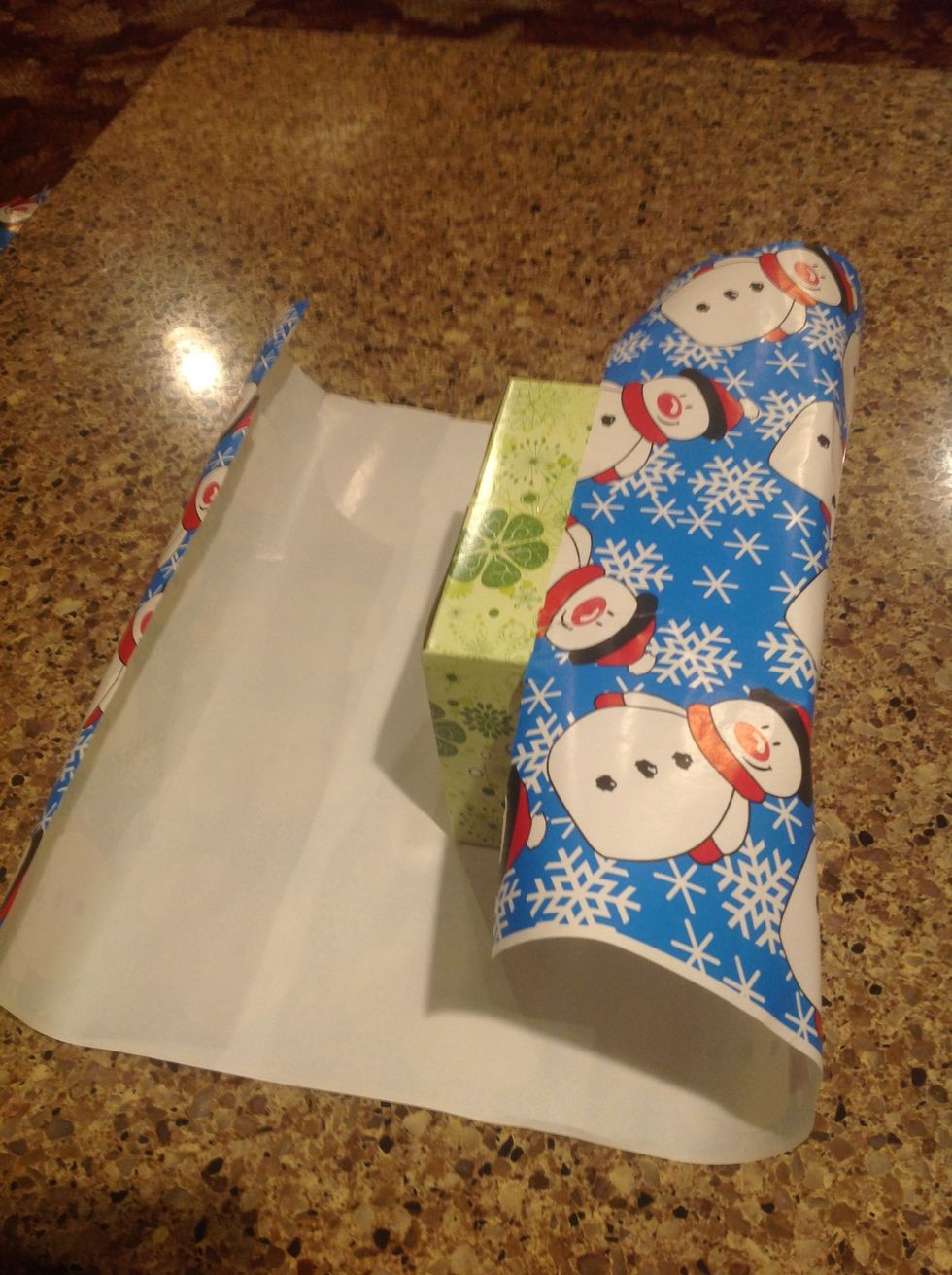 Next, making sure the gift is still centered, fold the paper over the gift on one side as shown in the picture.