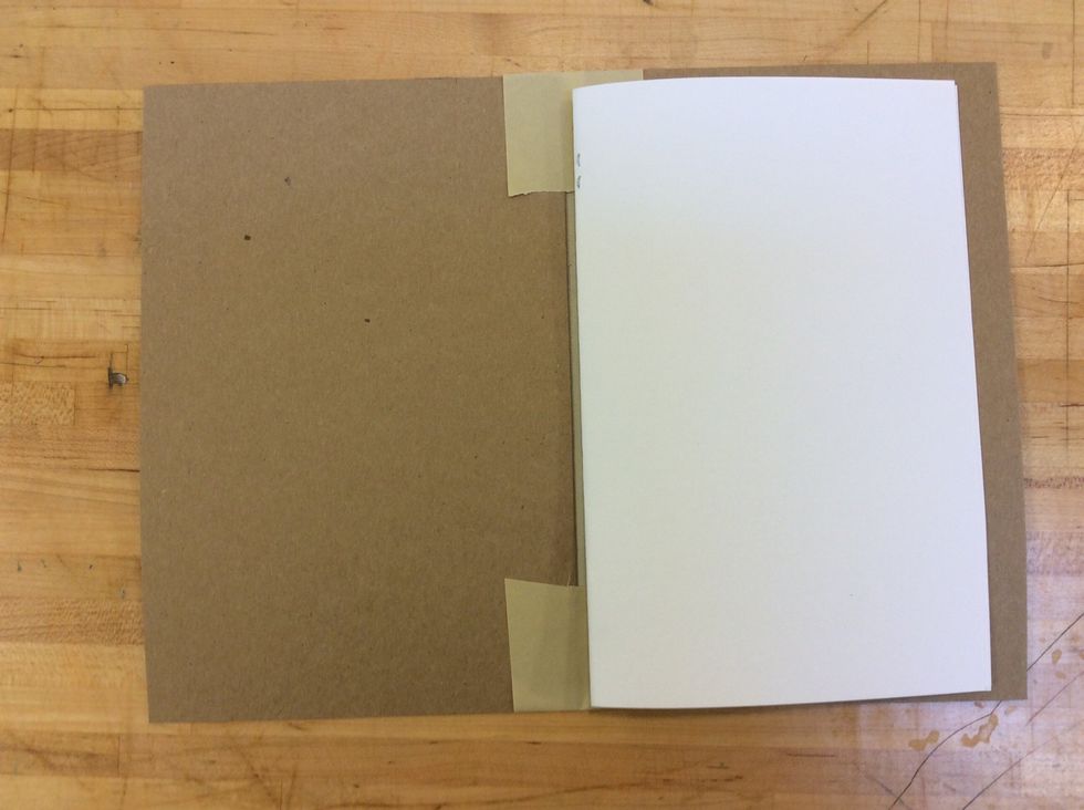 Next, open your cardboard cover and place your book lead on one side, with the staple edge in the center of your cover.