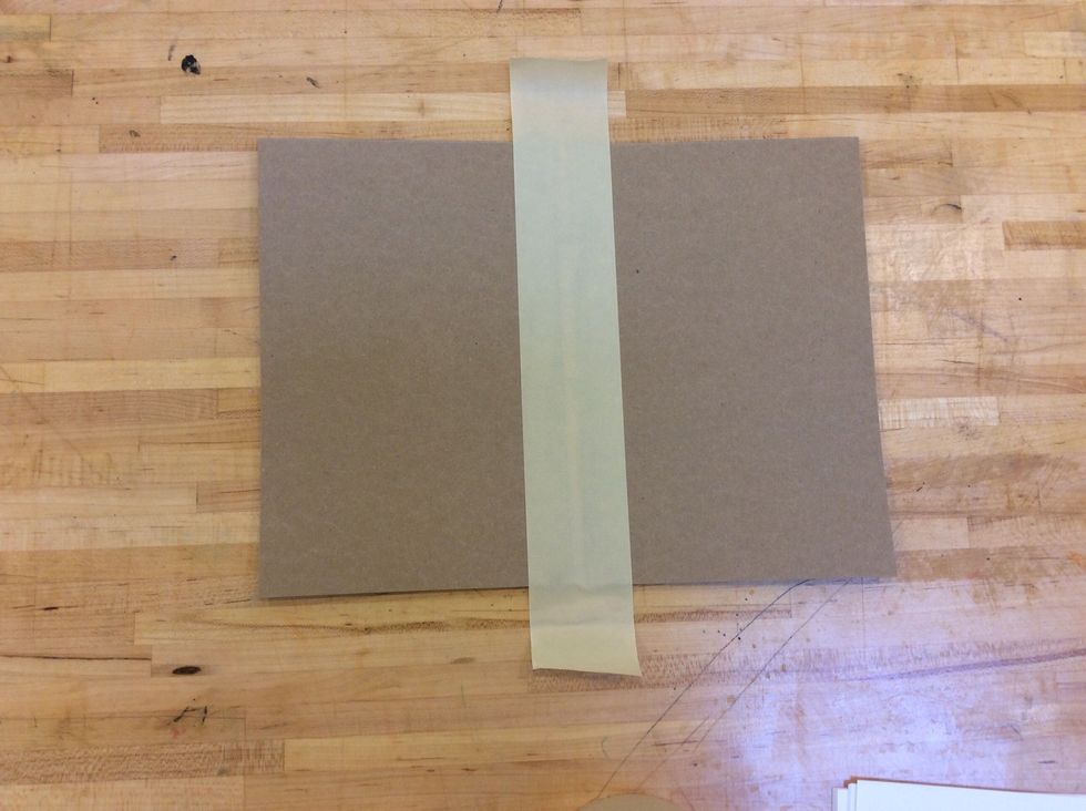 Next, put down a piece of masking tape in the center of the cardboard,covering both pieces equally. (The tape should extend past the top and bottom of the cardboard pieces)