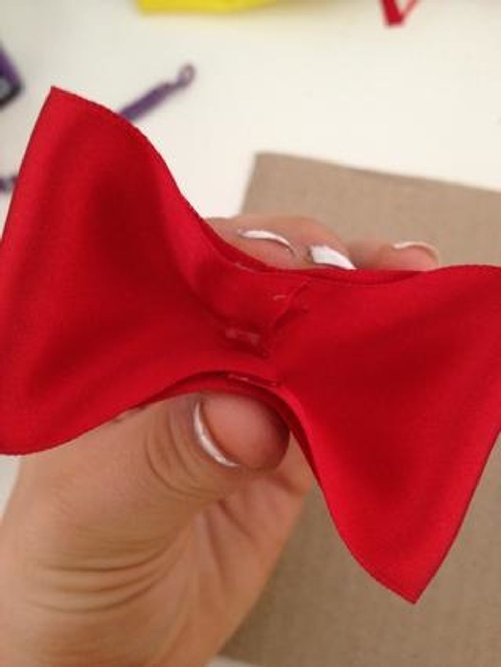 Next step, pick up your bow and squeeze the middle of your folded ribbon where you glued them together, as seen in the picture.
