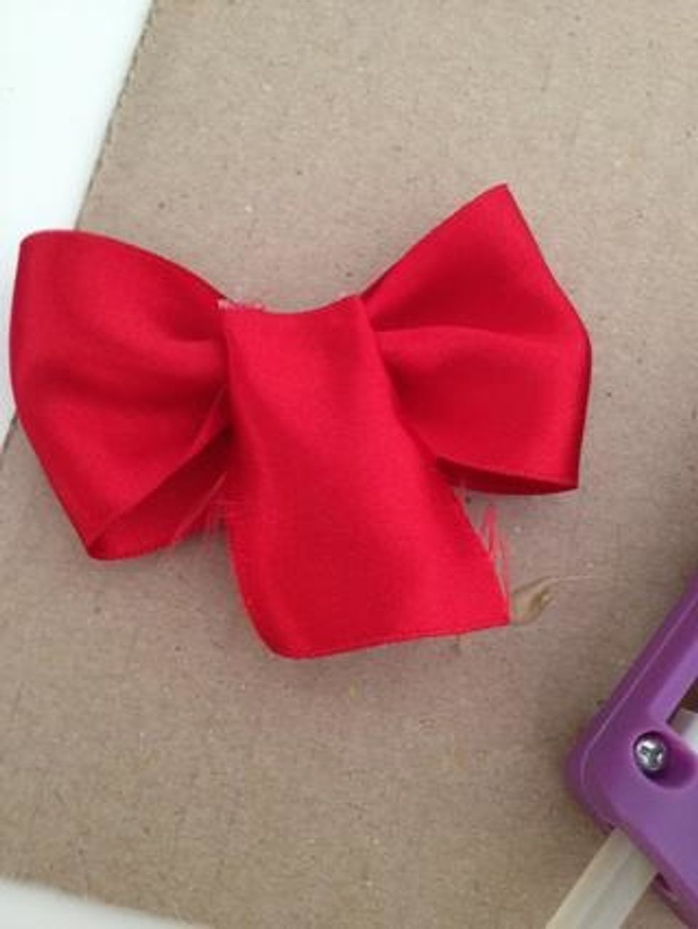 Next, take your folded piece of ribbon and wrap it around the crease of the bow, making sure to place the ended of the smaller ribbon in the area where you put hot glue in the previous step.