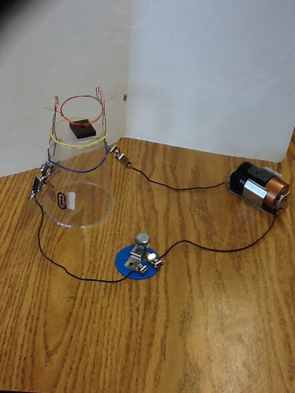Next we have the magnet on top of the center of the cup. Have the ends of the red coil sticking out of the loops of the copper wire. Have the coil on top of the magnet but not sitting on it.