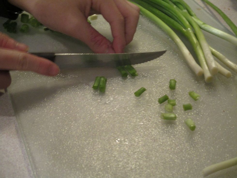 Next you chop the onions into small pieces with serrated knife and keep your fingers about 3 inches away from knife. Hold the Scallions with fingers.