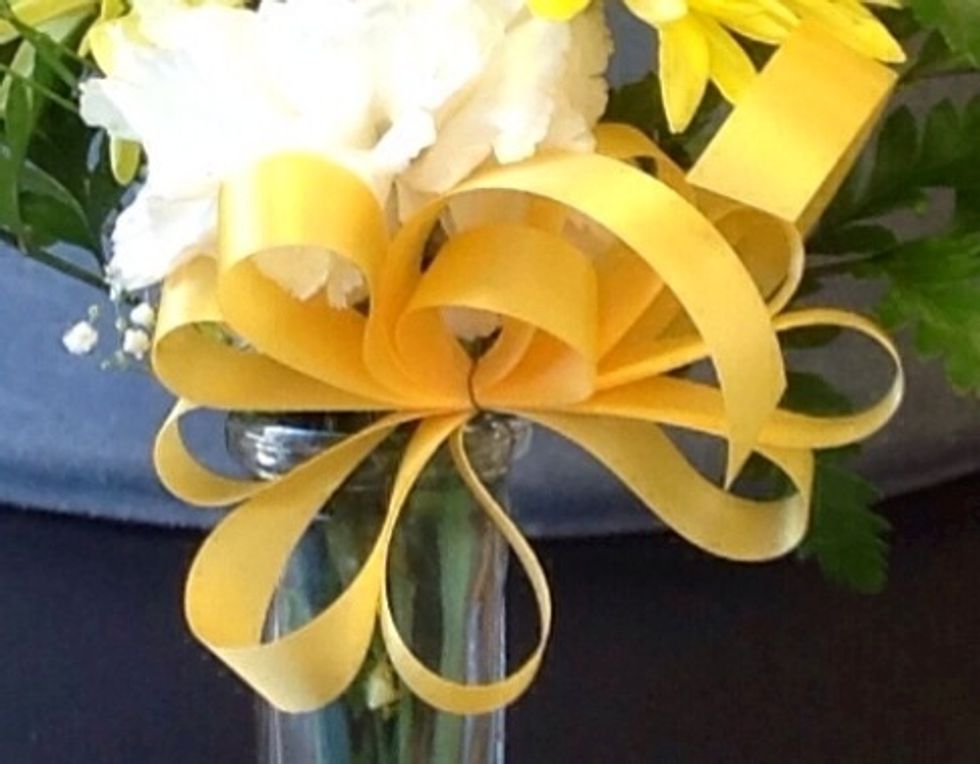 Next you will make a 123 bow. The bow should have five loops and it is secured to the bud vase by using florists wire. When making a 123 bow, use a piece of #3 ribbon that is an arms length long.