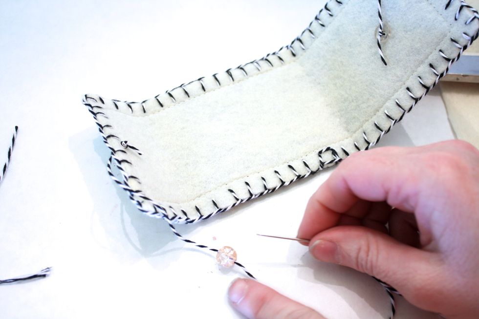 Now add a little decorative bead- close up your needle holder first to judge how much excess twine you need and where to tie the bead