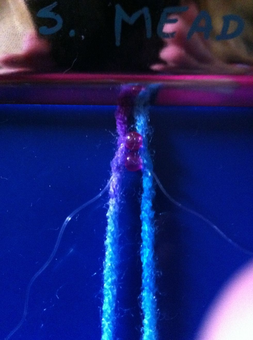 Now add the bead. To add the bead slip one end of the clear string through the bead hole closest to it. Do the same with the other string