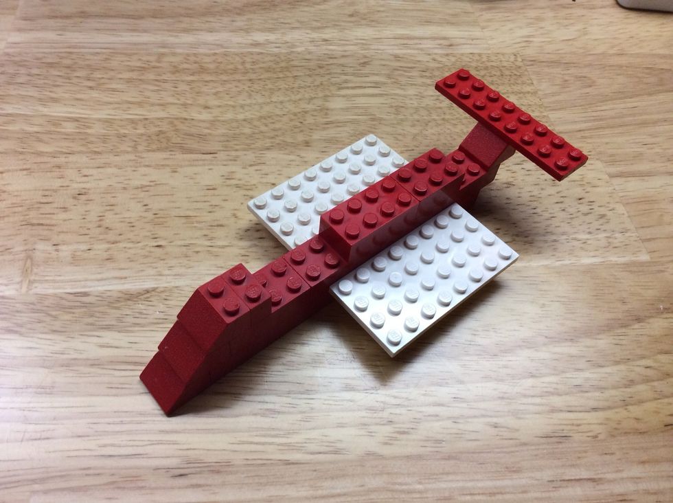 Now, add the two flat, white Legos to the two red base pieces on each side of the plane. Next, add the flat red piece to the rear, making a wing.