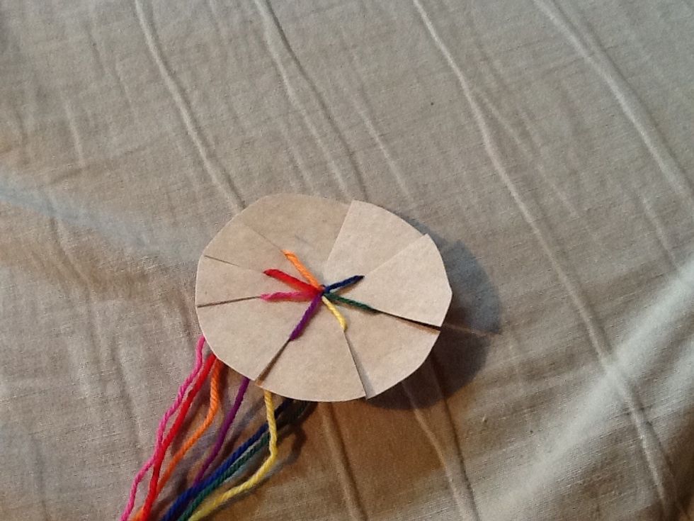 Now flip youre cartboard over so the knot is on the back. Then take youre pieces of yarn put Them into the cuts. Now there Will be one Cut that is free. And that is wery inportant.