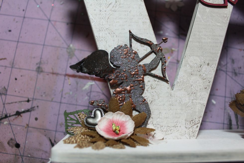 Now, I attached her to the piece and added some burlap flowers along with some pink flowers and a metal heart. I cut some card stock leaves using the Prima Forest leaves die.