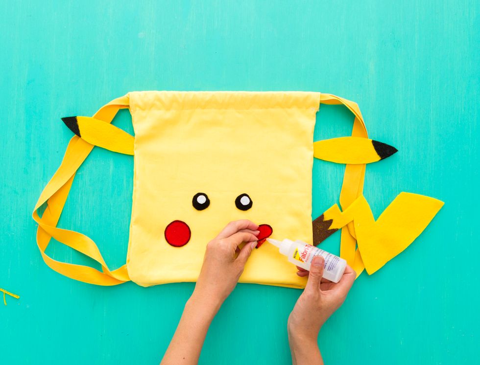 Now it's time to assemble. Attach the ears and tail to the backpack with your fabric glue. Then, glue the eyes and cheeks to the front of the backpack.