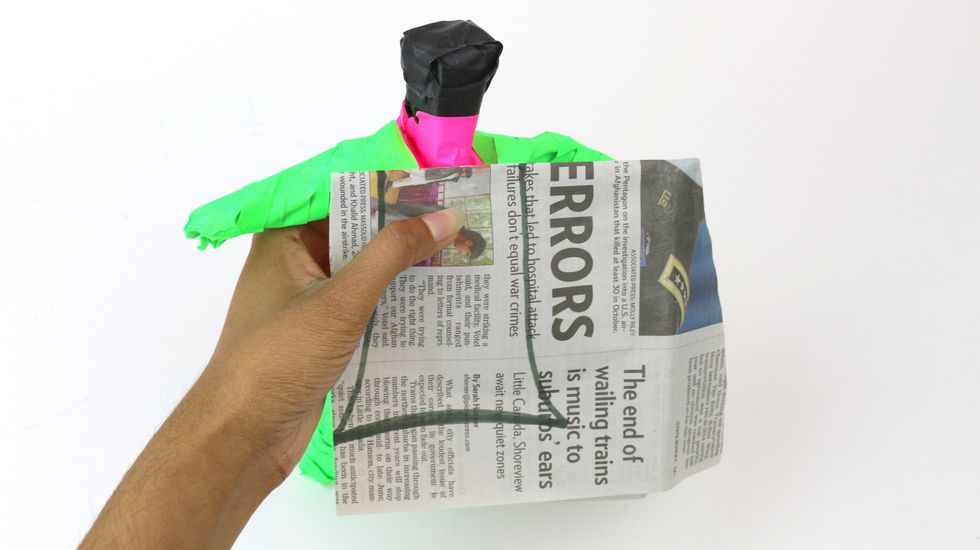Now, let's add a cape! Take another section of newspaper and hold it against the back of your figurine to measure the size of the cape. Using a marker, draw out the cape as big as you'd like!