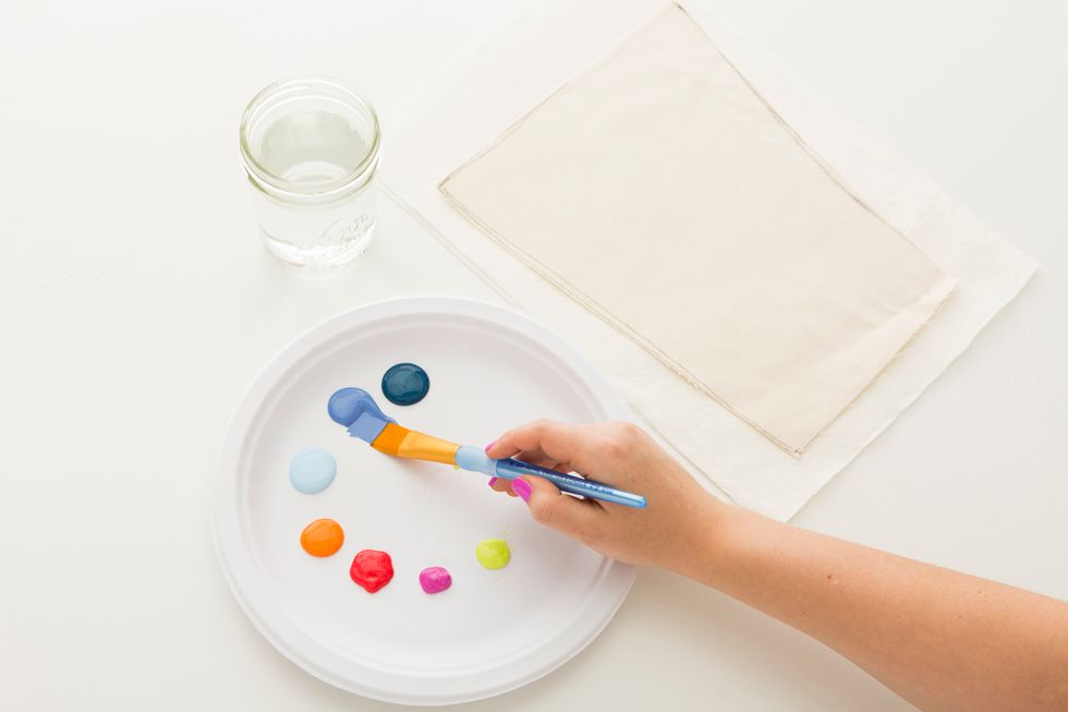 Now let\u2019s get painting! Squeeze out various colors of fabric paint onto a paper plate, lay your canvas panel on top of a paper towel and grab a jar of water to clean your brushes later.