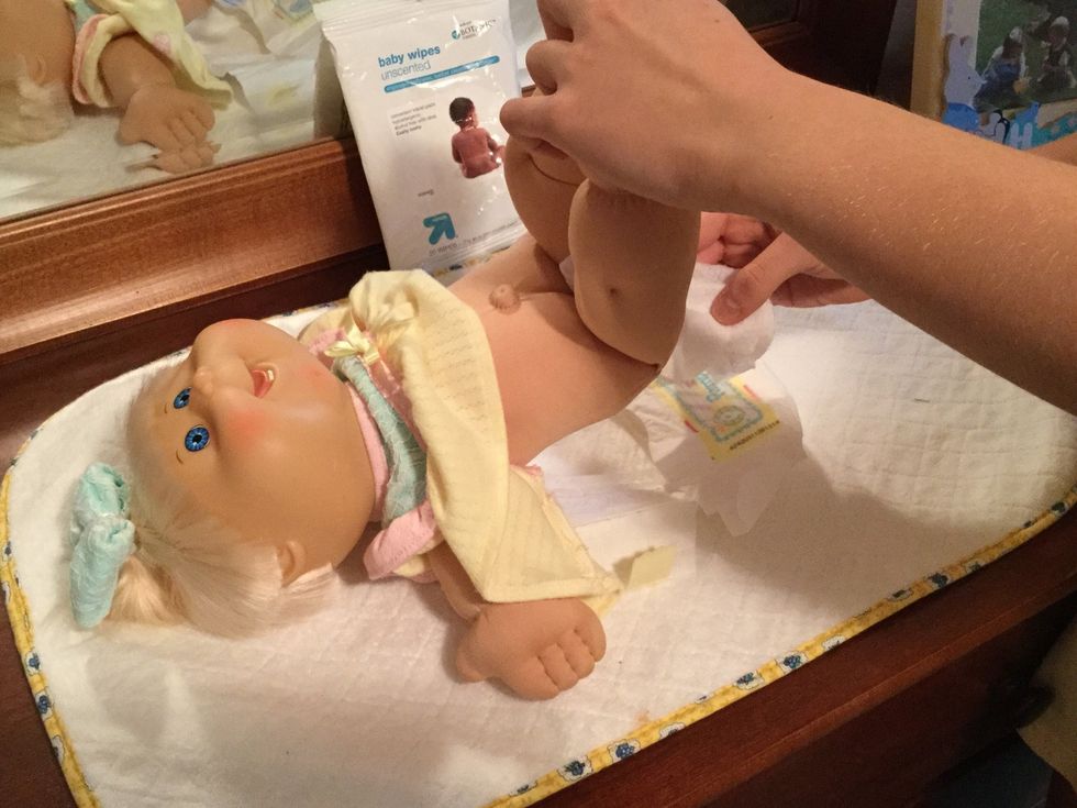 Now, making sure the diaper is folded underneath the child's  bottom, grab a baby wipe and clean the child's inner thighs and private parts.