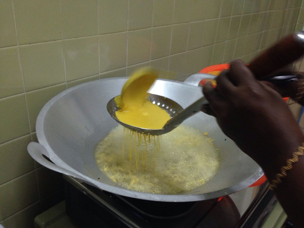 Now place the perforated ladle above the hot oil in wok and pour the batter straight into that perforated ladle from the deep ladle. And allow the droplets to flow directly in the hot oil.