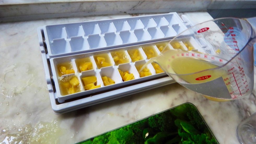 Now, pour in the freshly squeezed orange juice so that each ice cube hole is full and the mango cubes are fully submerged.