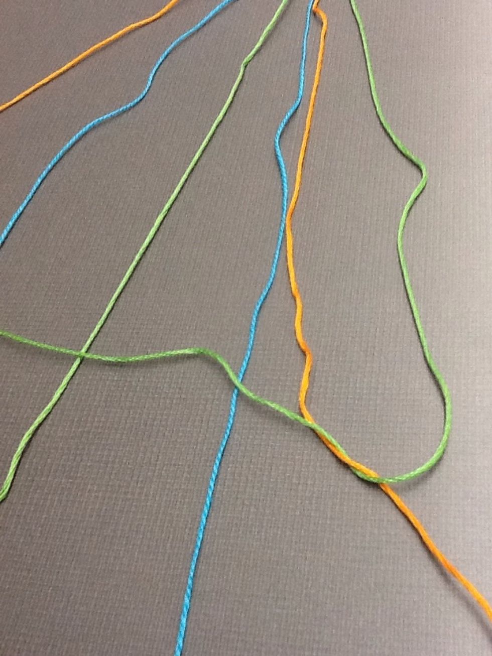 Now start doing the same thing to the other side. Working from the outside in, place the green string over the second colour(orange) then tie a knot