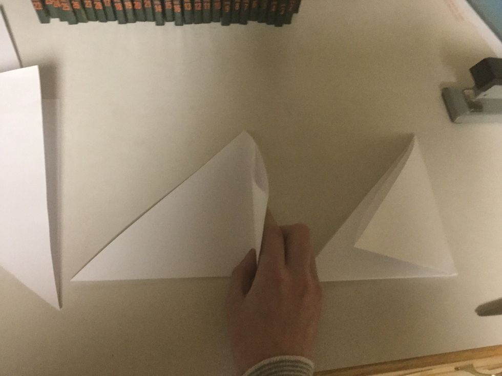 Now, take a paper triangle and fold it in half into a smaller paper triangle. Repeat this with each piece of paper.